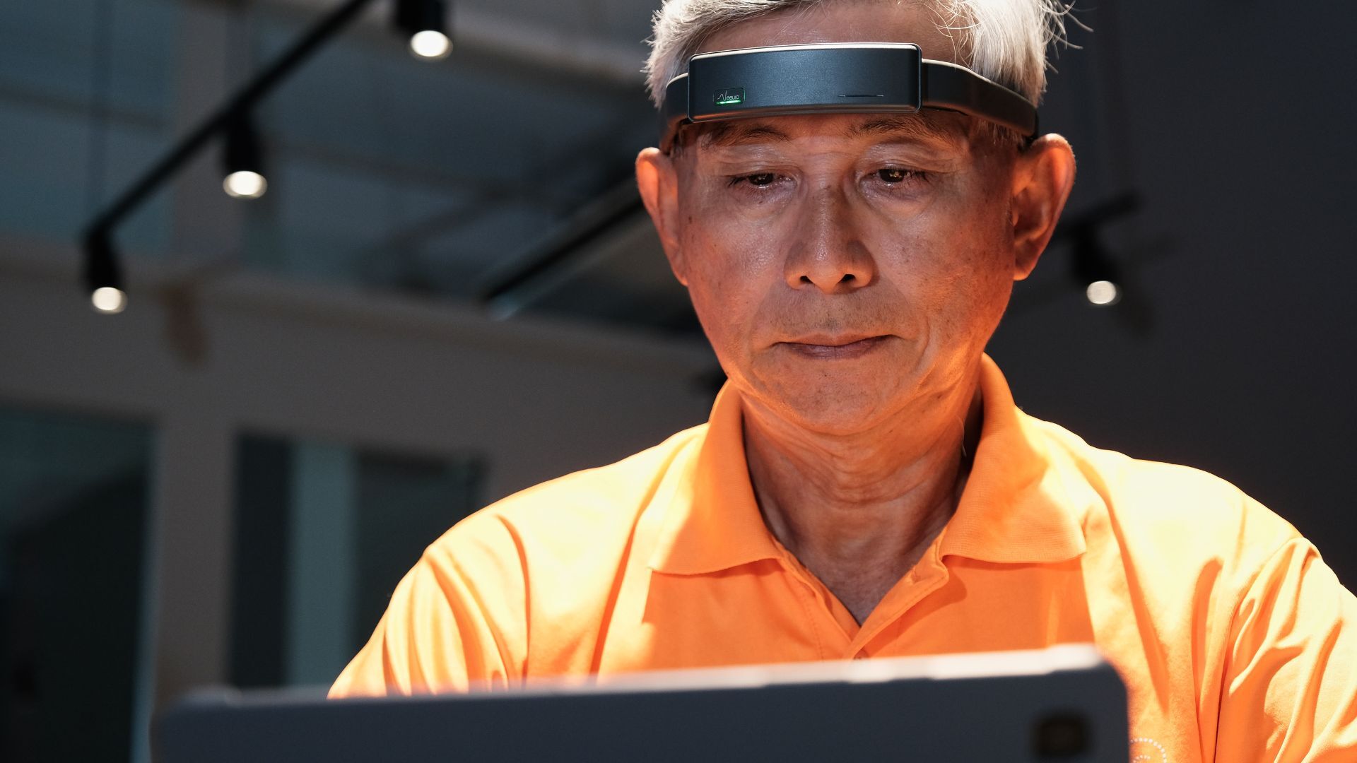 A senior user wearing an EEG headband while focusing on a tablet-based cognitive task, illustrating brain-activity monitoring, attention training, and healthy aging through neurotechnology.